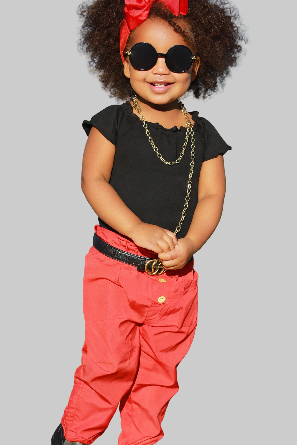 Child wearing a black top, red pants, and sunglasses on a street.