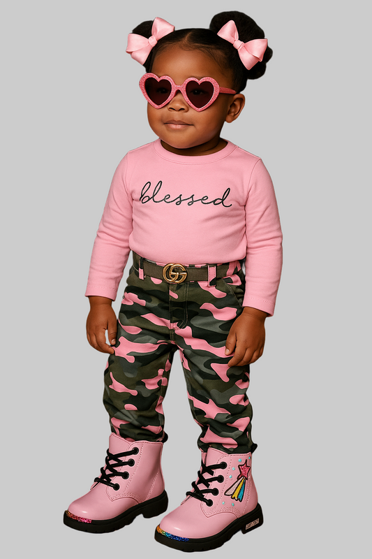 Child wearing a pink 'blessed' shirt, camouflage pants with pink accents, and pink boots with heart-shaped sunglasses against a black background.