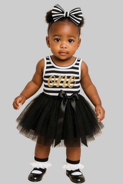 Baby girl in a black and white striped dress with a tutu and bow headband on a plain background