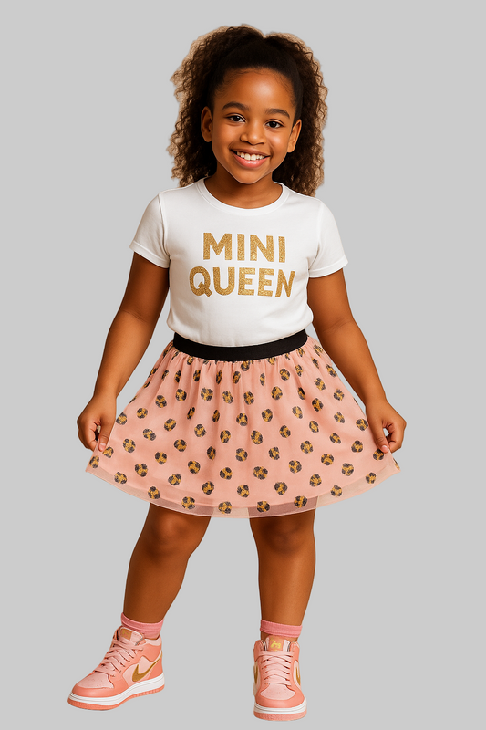 Young girl wearing a 'MINI QUEEN' t-shirt and pink skirt with gold accents on a beige background