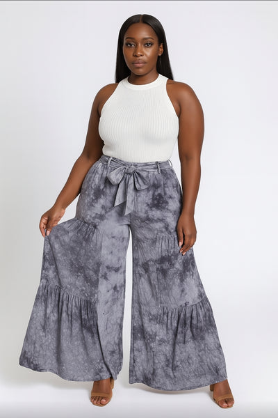 Woman wearing a white sleeveless top and gray tie-dye wide-leg pants on a white background