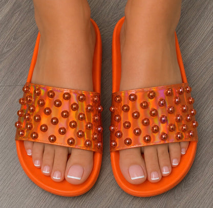 Orange sandals with bead embellishments on a wooden floor