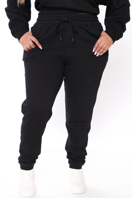 A woman standing and posing in black Nova sweatpants with an elastic waistband and drawstrings.