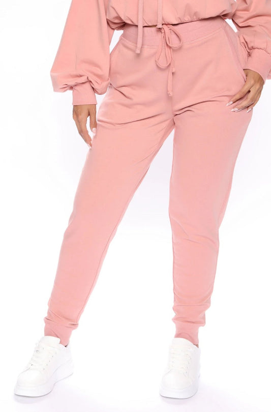 A woman standing and posing in mauve pink tapered sweatpants with an elastic waistband, paired with white sneakers.