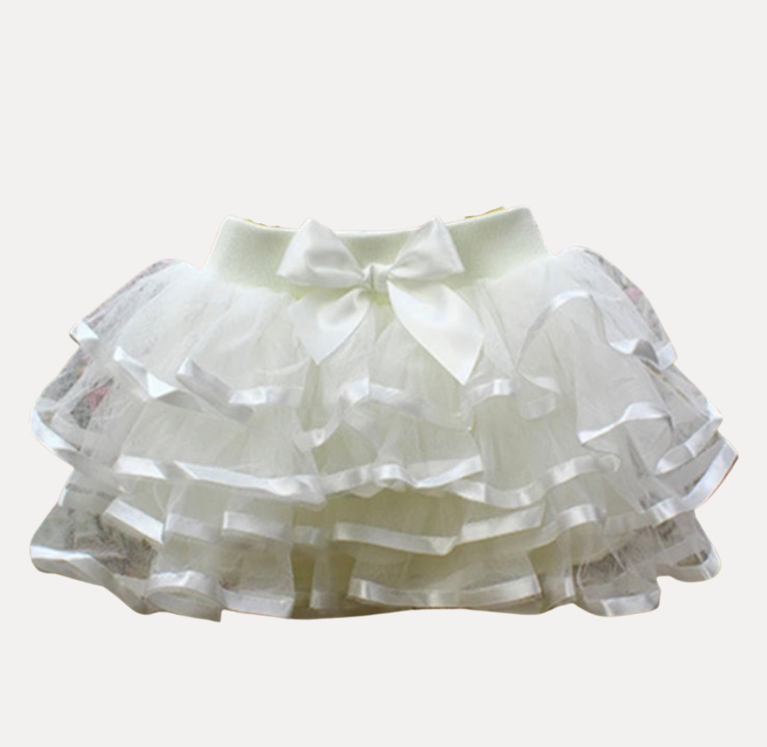 A pink tutu skirt with white ruffles and a front bow detail, designed for girls.