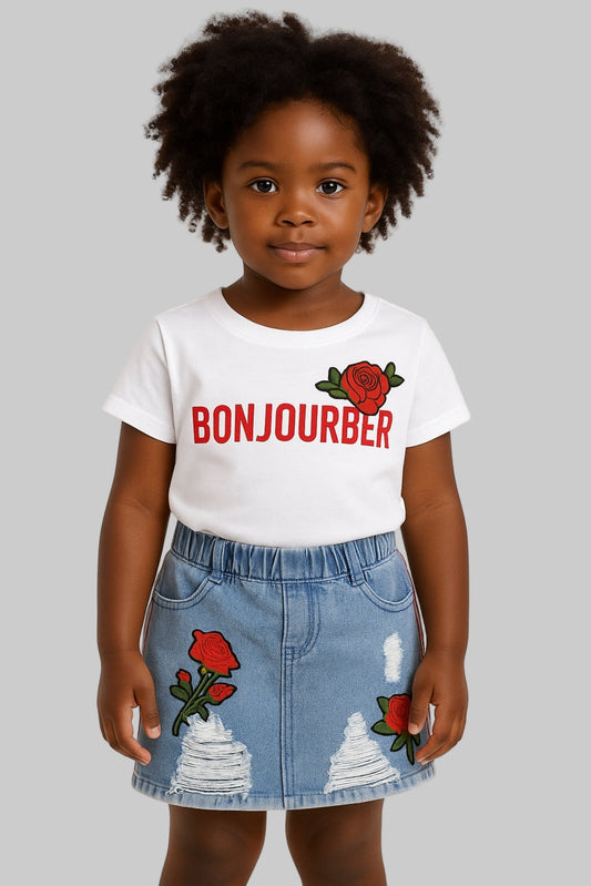 Child wearing a white t-shirt with 'Bonjourber' and a denim skirt with rose designs on a plain background