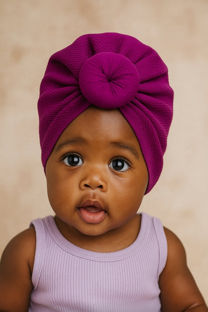Baby wearing a purple turban against a beige background