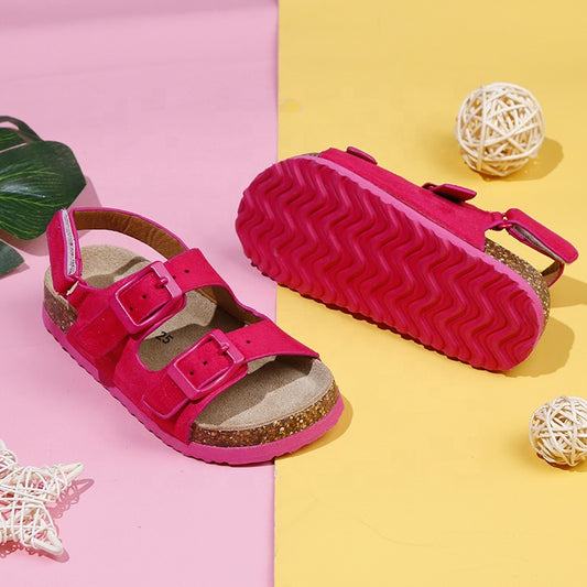 A pair of brown unisex retro sandals with adjustable velcro straps and a textured sole, displayed on a colorful background with a few decorative items.