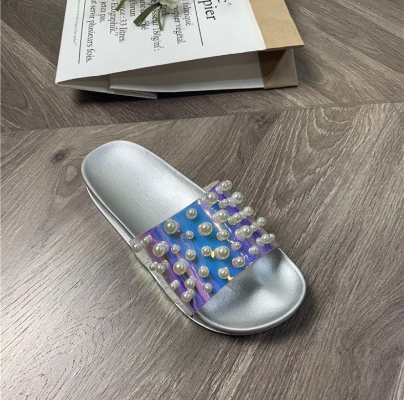 Silver slide sandal with purple and blue design and pearl embellishments on a wooden floor.