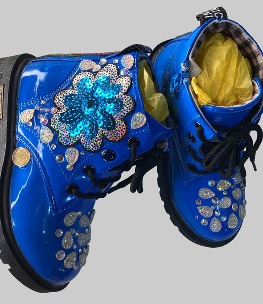 A pair of blue ankle boots for kids with decorative rhinestones and a graphic design, displayed on a white furry surface.